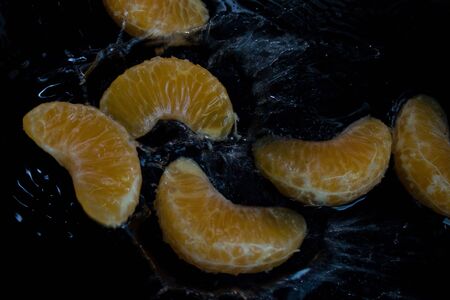 Pieces of tangerine fall into the water, which splashes around.Dark photo of fruit falling into water and drops splashing around.の写真素材