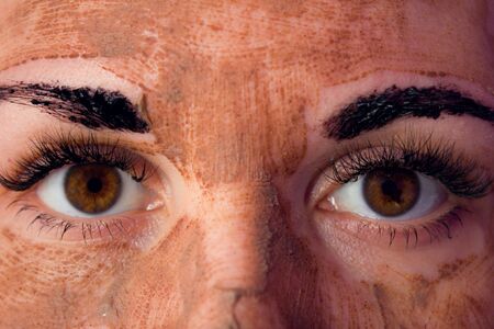 Beauty day. Close-up of a woman`s face. The woman has a clay face mask and eyebrows painted black.の写真素材