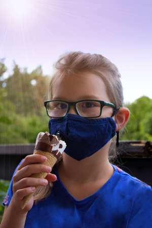 Anti covid mask as a barrier when licking ice cream. Girl in blue mask  holding ice cream in hot...