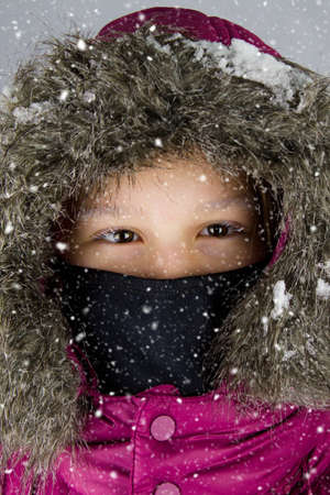 The little girl in a purple winter coat has a snow on a hood. Her lashes are frozen and her mouth protects the respirator against covid 19. Close up of a little girl with white eyelashes and a hood.の写真素材