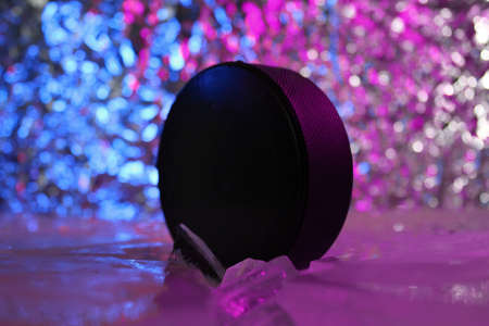 Hockey puck stands on the edge in cracked ice. A lilac blue light falls on him. Hockey concept.の写真素材