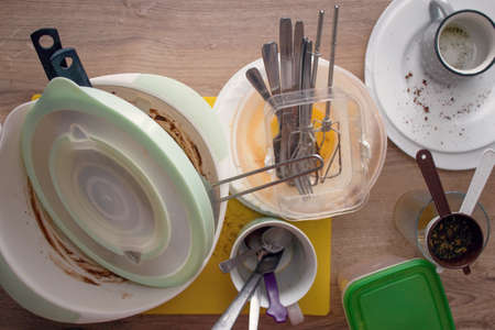 Dirty dishes stacked on the kitchen counter waiting to be washed.Unwashed plates, bowls and dishes, cutlery, cups, glasses, strainers and cutting board on the kitchen worktop.の写真素材