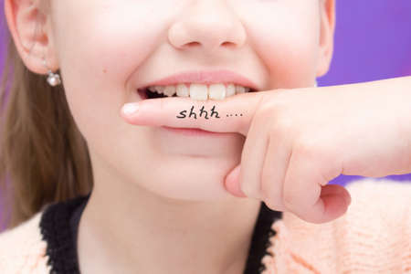 Keep a secret. Don`t tell anyone.A young girl has forefinger in her mouth and the inscription Shhh...