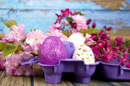 Four eggs decorated with wax and glitter in a purple egg wrapper and branches of ornamental...