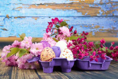 Four eggs decorated with wax and glitter in a purple egg wrapper and branches of ornamental...