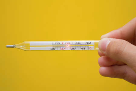 The mercury thermometer shows 38 Â° C. The thermometer in hand in front of a yellow background.の写真素材