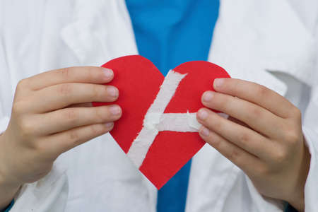 A doctor holds red paper heart stuck with plaster.Concept on the theme of heart disease, surgery and a healthy lifestyle good for our cardiovascular system.の写真素材