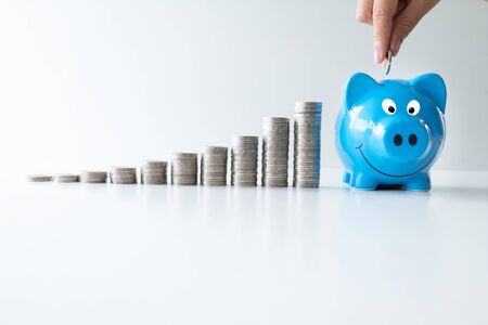 hand putting coin into blue piggy bank with coins graph, step up start up  business to suscess, Saving money for future plan and retirement fund concept.の写真素材
