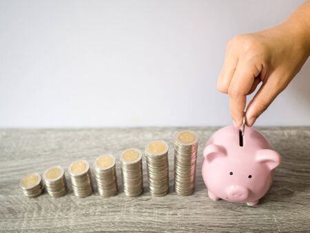Woman hand putting coin into pink piggy bank with coins pile growth graph, saving money for future investment plan and retirement fund concept.の写真素材