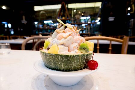 Mixed fruit salad in a melon, decorated with cherries Ready to serve in a white bowl.