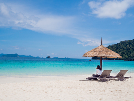 Business women sitting on seat and sun shelter on white sand beach sea view background, Travel plans in holidays or after retirement .のeditorial素材