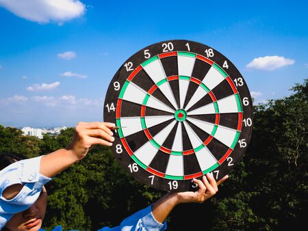 Businesswomen hand holding dart Board on blue sky and city view background, Setting challenging business goals And ready to achieve the goal concept.の写真素材