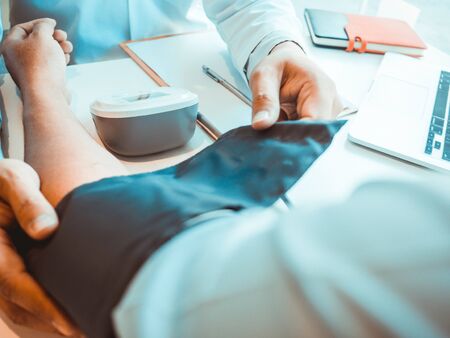 The doctor evaluates the patient with a stethoscope, blood pressure monitor and records the results.の写真素材