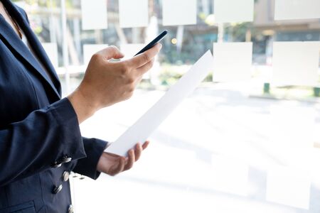 Business woman used smartphone and holding paper at the office room, Setting challenging business goals and ready to achieve the target concept.の写真素材