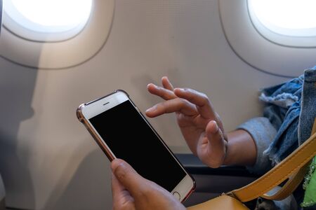 The woman's hand sitting by the window on the plane playing smart phone.