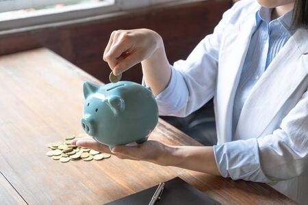 Business woman putting coins into blue piggy bank, saving for new business target and retirement concept.の写真素材