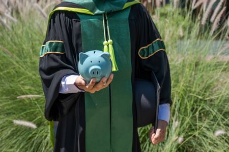 The person in the bachelor uniform  hoding blue piggy bank, Saving money for education plan and retirement fund concept.の写真素材