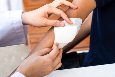 The doctor is treating the wound on the elbow of the patient.