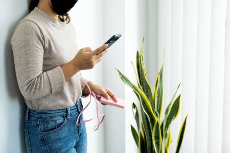 Young women in mask leaning against the wall playing with smartphone While charging the smartphone...