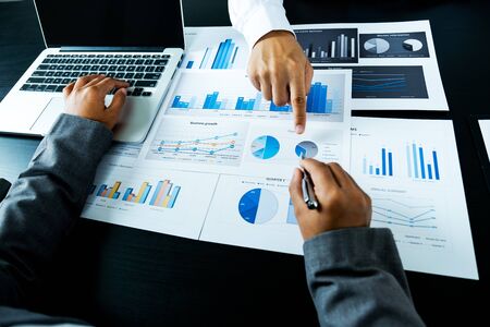 businessmen and businesswomen team pointing to charts meeting to plan strategies to increase...