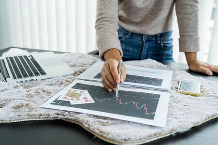 Young women sitting at a desk with a laptop, stock chart and cards, Don't play stockshare like gambling concept.の写真素材