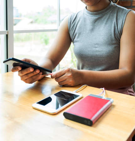 Young women sitting on the chair playing with smartphone While charging the smartphone battery and...