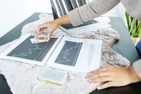 Young women sitting at a desk with a laptop, stock chart and cards, Don't play stockshare like gambling concept.の写真素材