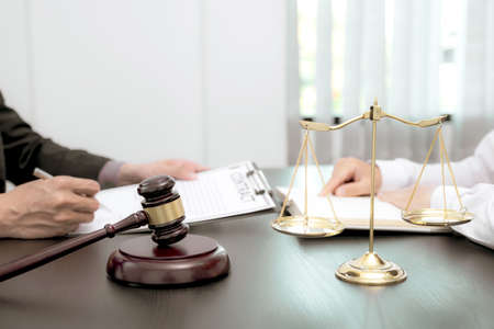 The scales of justice and judges gavel standing in front of the male lawyer who is providing service...