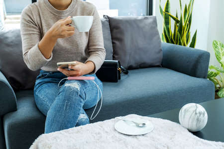 Young woman sitting on the sofa drinking coffee and mobile phone chargers.