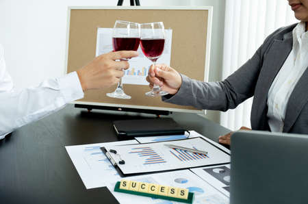Two business executives people,businesswomen, and businessman in a suit is bumping into a glass of wine celebrating success at the office desk. After the meeting.の写真素材