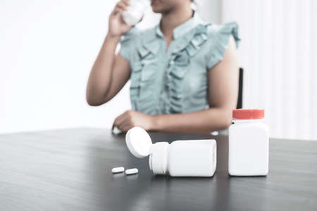 Bottles of medicine stands on the table in front of a young woman in Asia taking pills, vitamins, and capsules to help get sick and stay healthy.の写真素材
