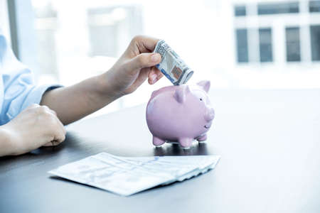 Woman putting dollar banknotes into piggy bank, step up start up business to success, Saving money for future plan and retirement fund concept.の写真素材