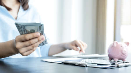 The woman's hand holding the dollar note and there is a piggy bank on the table, step up start up...