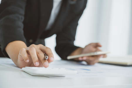 businesswomen bookkeeper use calculator and laptop doing account for paying tax on white desk in...