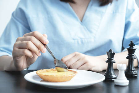 Woman hand in blue dress scoop eating egg tart with a spoon.