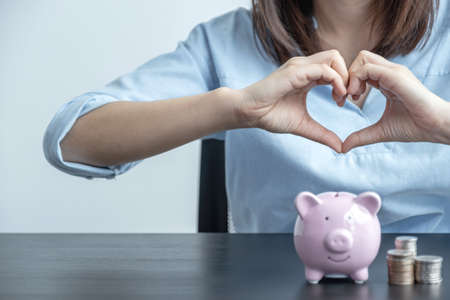 Woman hands making heart shape over pink piggy bank, step up start up business to success, Saving money for future plan and retirement fund concept.の写真素材