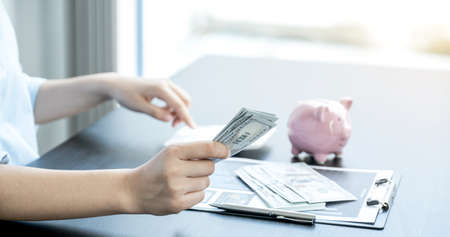 The woman's hand holding the dollar note and there is a piggy bank on the table, step up start up...