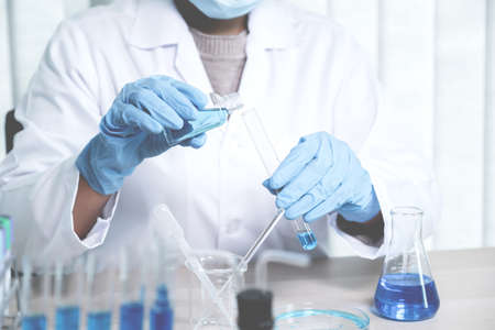 Scientists hold a glass tube filled with blue chemical liquid for research and analysis in a...