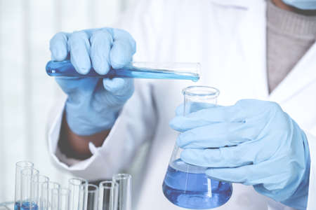 Scientists hold a glass tube filled with blue chemical liquid for research and analysis in a...