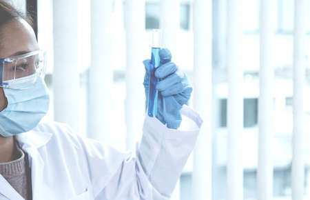 Scientists hold a glass tube filled with blue chemical liquid for research and analysis in a...