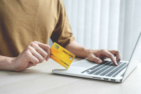 Businessman hand hold credit card to online shopping on laptop computer from home, payment e-commerce, internet banking, spending money.の写真素材