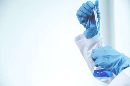 Scientists hold the pipette and drop the blue chemical liquid for research and analysis in a...