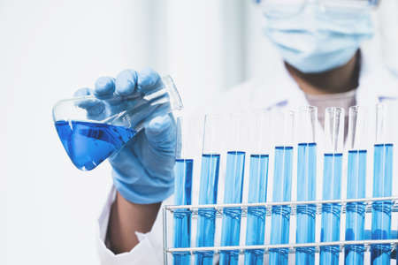 Scientists hold a glass filled with blue chemical liquid for research and analysis in a laboratory.