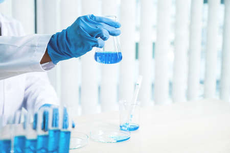 Scientists hold a glass tube filled with blue chemical liquid for research and analysis in a...