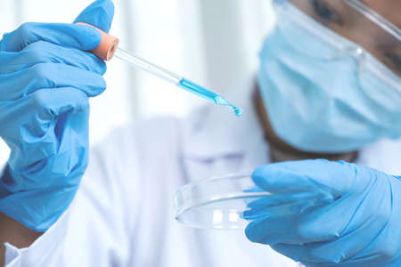 Scientists hand hold the pipette and drop the blue chemical liquid for research and analysis in a...
