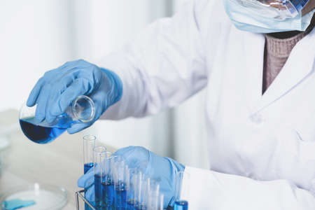 Scientists hand hold a glass filled with blue chemical liquid for research and analysis in a...