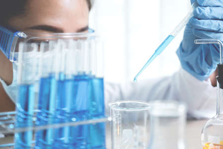 Scientists hand hold the pipette and drop the blue chemical liquid for research and analysis in a...