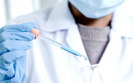 Scientists hold the pipette and drop the blue chemical liquid for research and analysis in a...