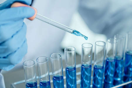 Scientists hold the pipette and drop the blue chemical liquid for research and analysis in a...