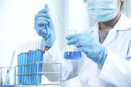 Scientists hold the pipette and drop the blue chemical liquid for research and analysis in a...